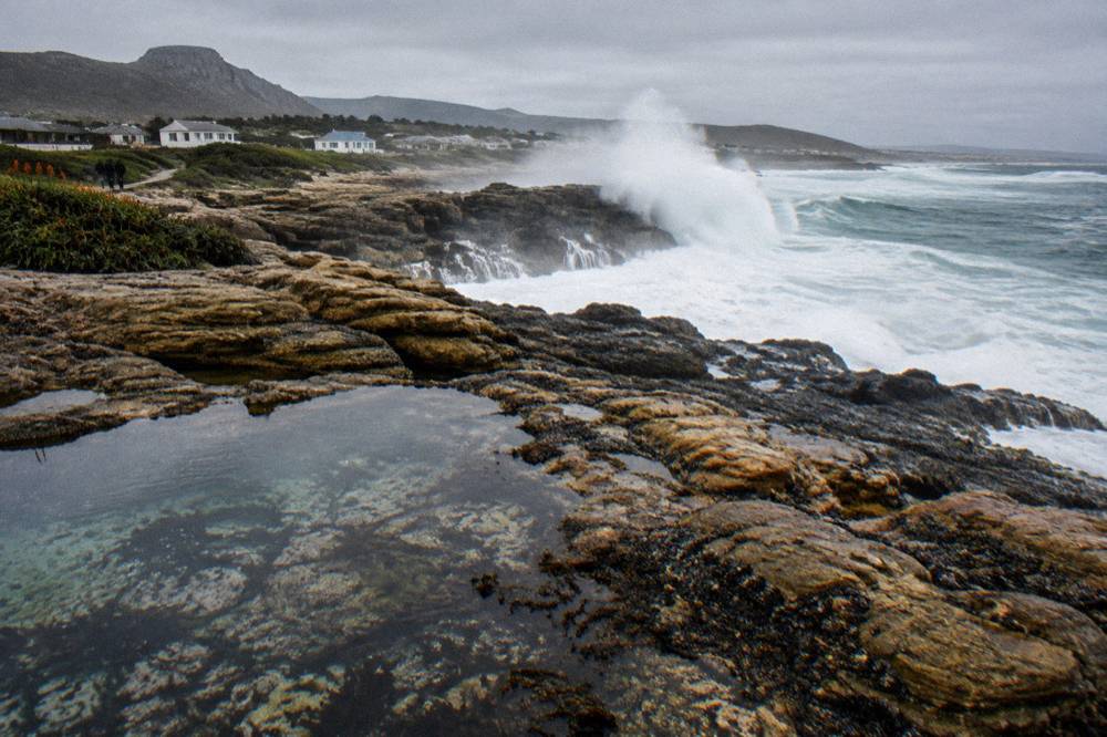 Heavy ocean swell breaking near a rocky headland under grey sky
