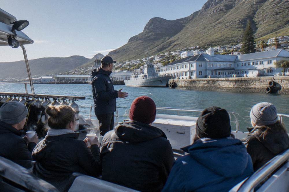A dive crew member briefing passengers on the deck of a shark diving boat in Simon's Town harbour