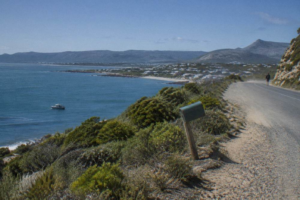 A coastal road winding along cliffs above a calm bay with a distant boat