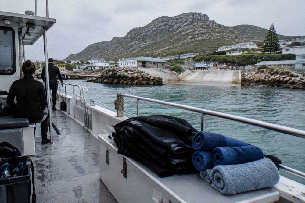 Folded wetsuits and towels laid out on a boat deck under overcast sky