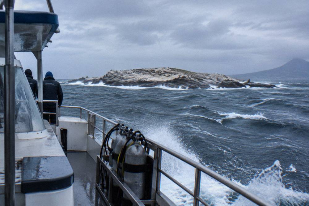 A dive boat anchored near a rocky island in rolling swell with whitecaps on the water
