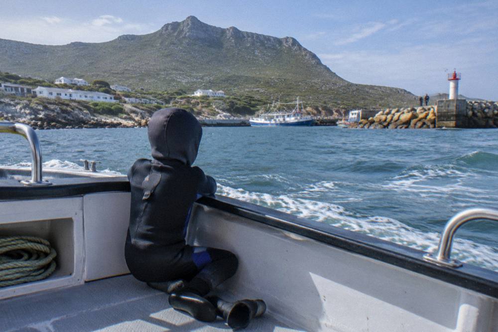 A child in a wetsuit sitting on a boat bench looking out toward a rocky island