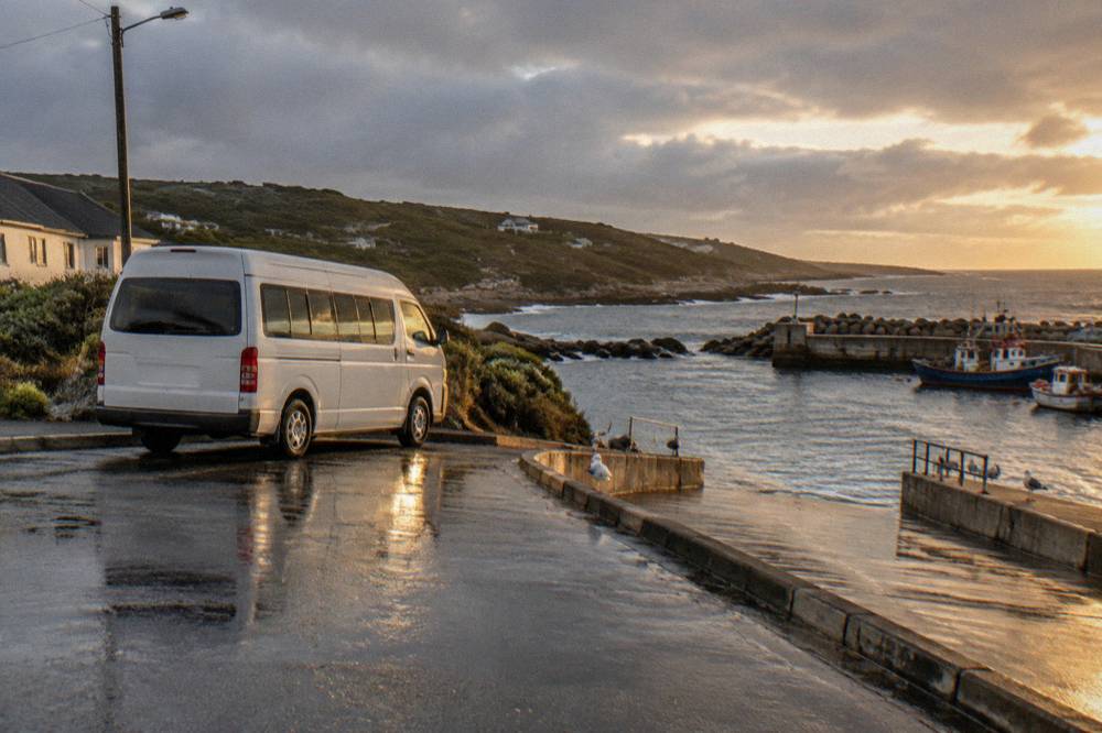 A minibus parked on a harbour road with the sea behind it
