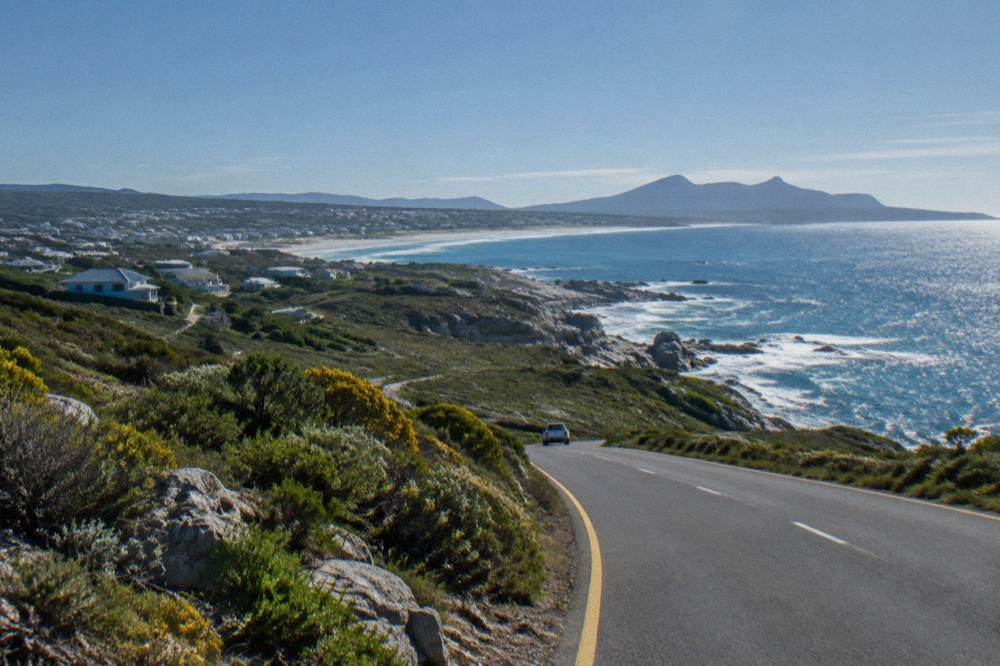 A coastal road winding along cliffs above the ocean toward a distant bay