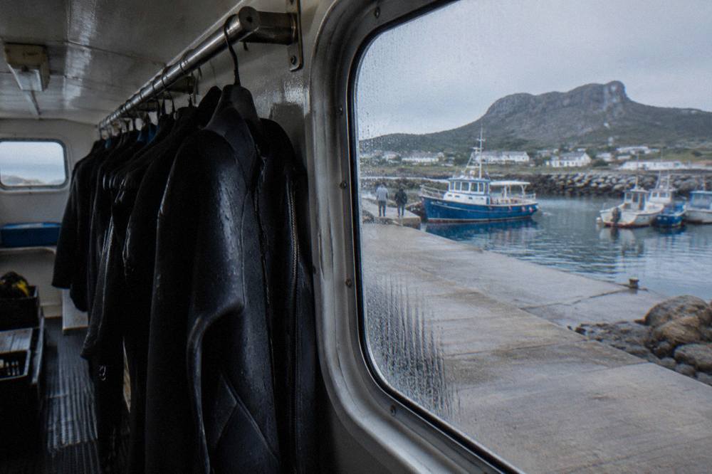 A rack of black neoprene wetsuits hanging inside a shark diving boat cabin