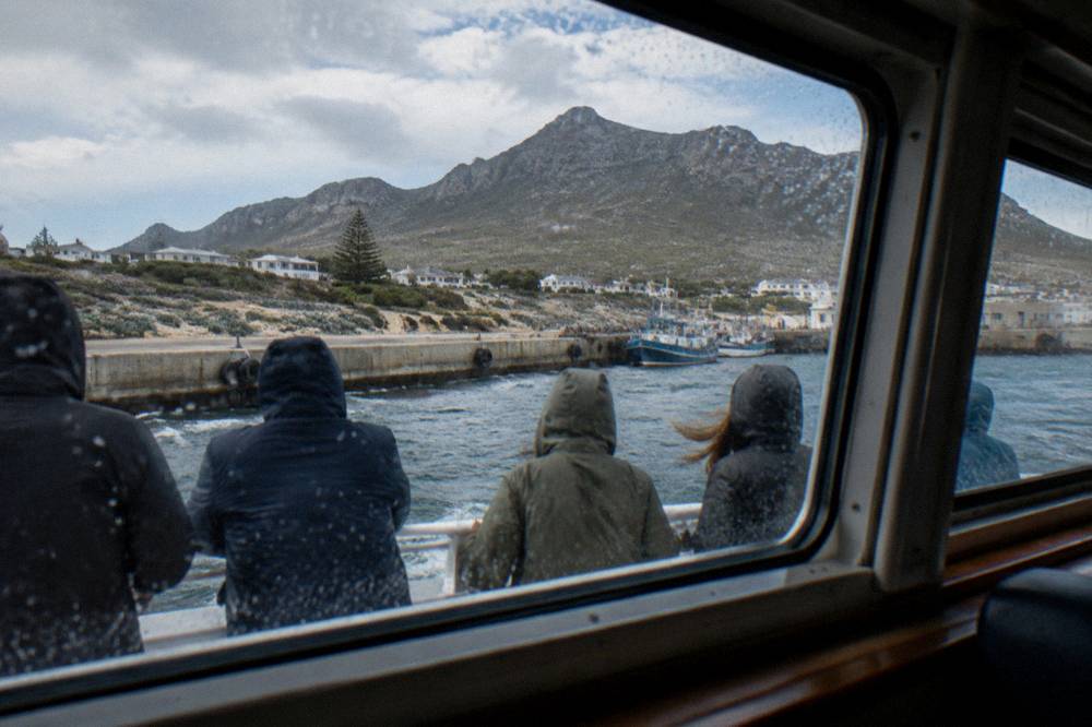 Passengers in windproof jackets and warm hats seated along the rail of a shark diving boat